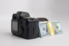 Three stacks of dollar bills, with a digital DSLR camera